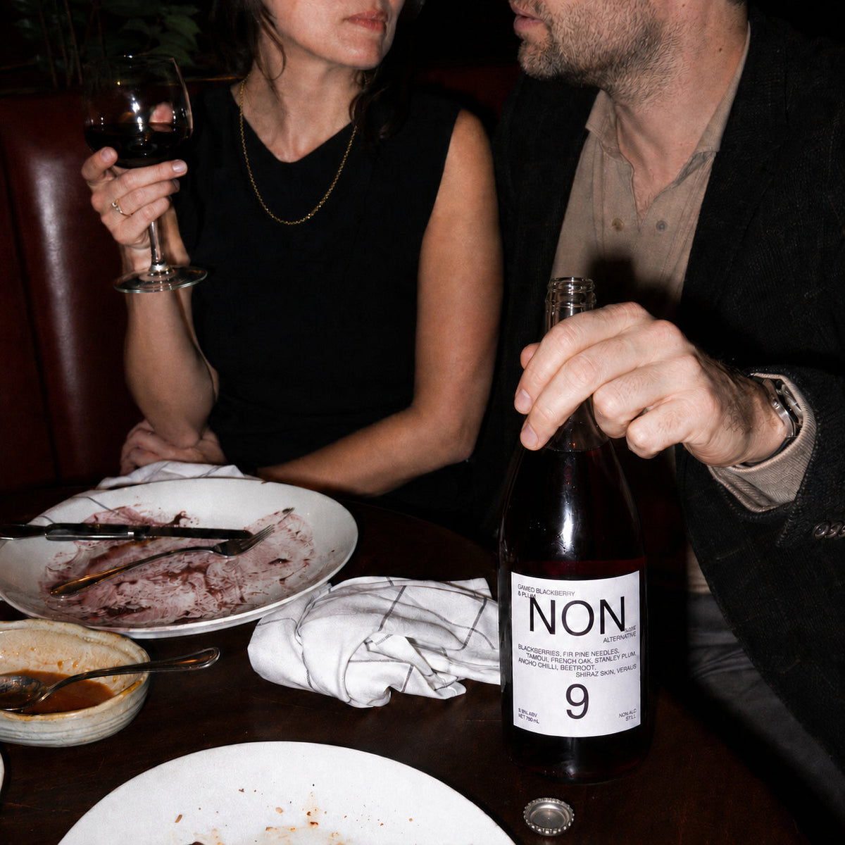 NON9 Oaked Blackberry and Plum bottle on a restaurant table beside two diners